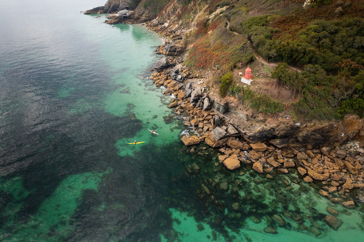 Landscape picture of people kayaking over clear waters next to rocky cliff