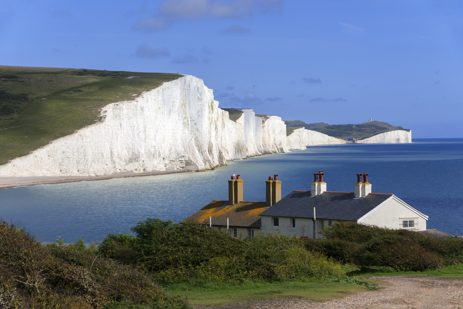 House looks over view of white cliffs next to blue ocean - South Downs Way, Sussex