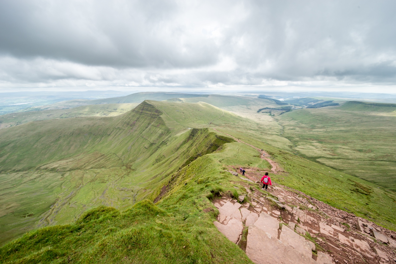 People walk down rocky steep path with views over Pen y Fan's green landscape - Climbing Pen y Fan
