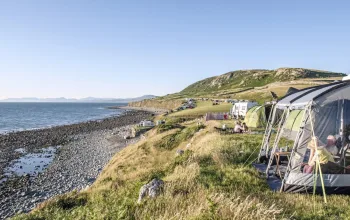 Tents pitched on hillside next to beach with pebbles Campsites in Snowdonia CREDIT Cae Du Farm Holidays Campsite