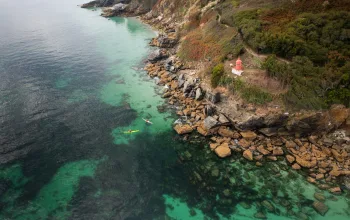 Landscape picture of people kayaking over clear waters next to rocky cliff Brittany CREDIT Jake McKenna