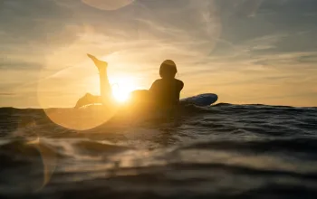 Silhouette of woman on surfboard with leg in the air and sunset in the background Surf Camp CREDIT Sam Haddad