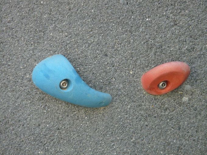 A blue and a red edge climbing hold on a grey concrete wall