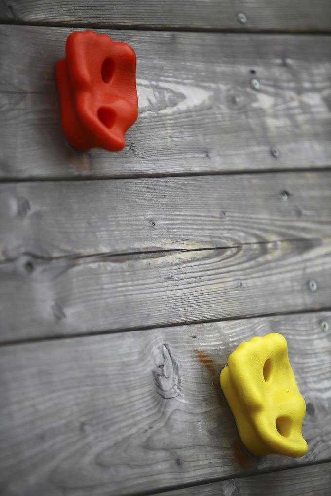 A red and yellow climbing hold on a grey wooden wall