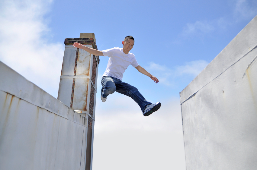 Asian young man making a giant leap in between buildings