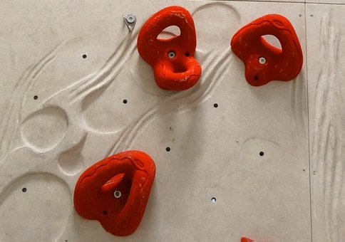 Red jug climing holds on a white climbing wall