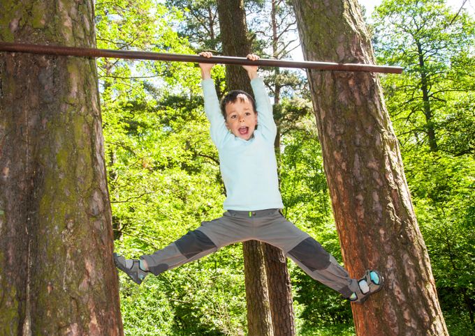 Child hanging off a metal bar in a forest