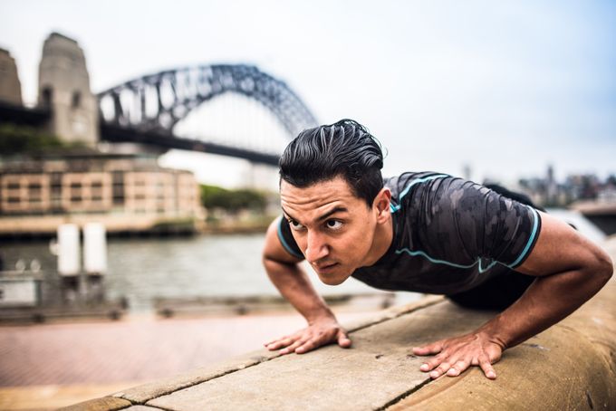A man doing a press up on a wall outside with a bridge in the background