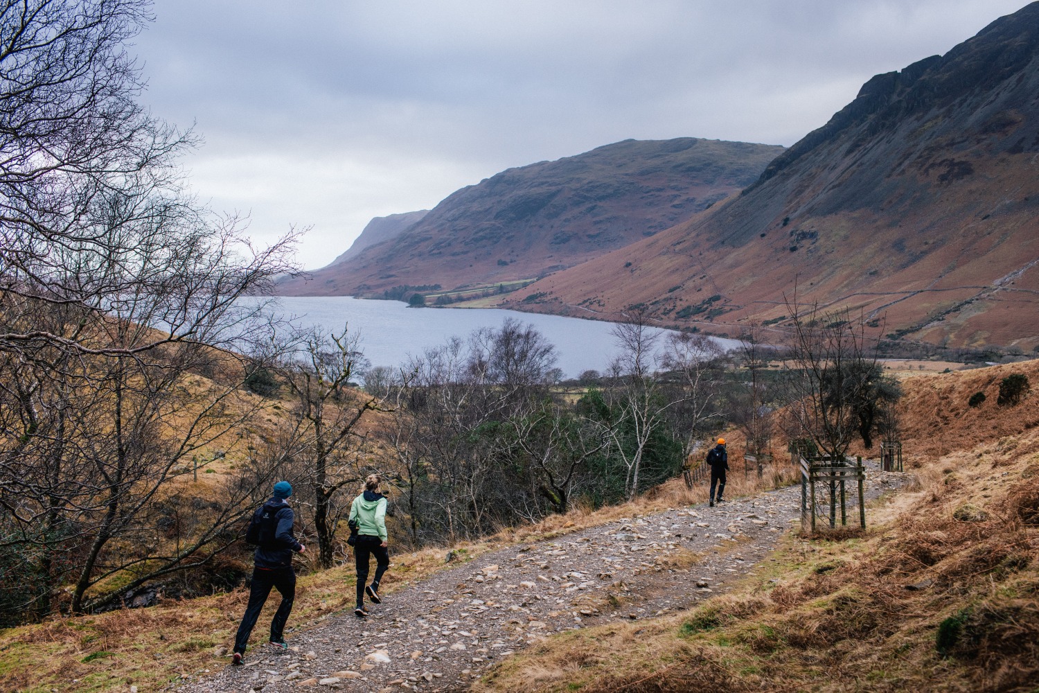 People running along path next to lake with hills in background - Lake District