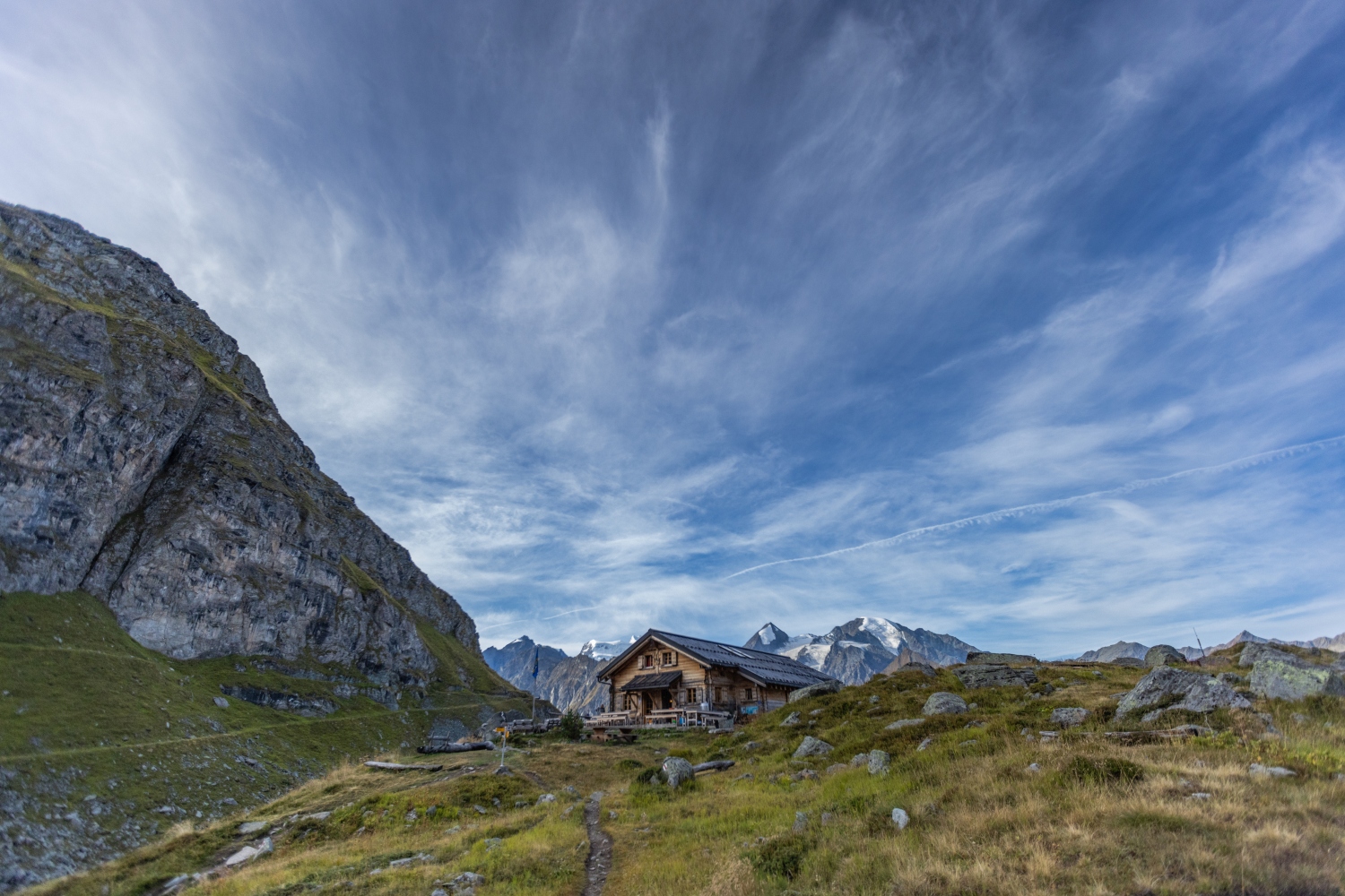 Hut at top of rocky hill with snow capped mountains in background - Verbier
