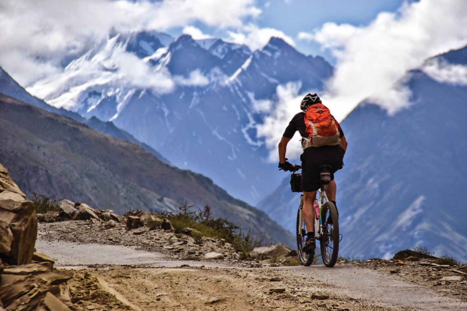 Man cycling along rocky road with mountains in background, Himalayan Mountains