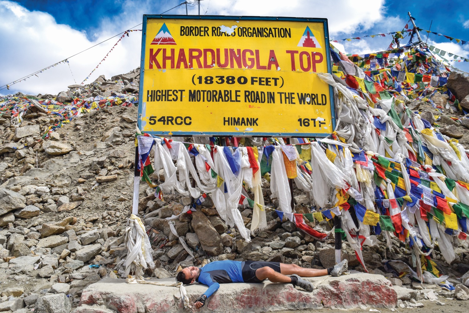 Man lying below "Khardungla Top" sign, Himalayan Mountains