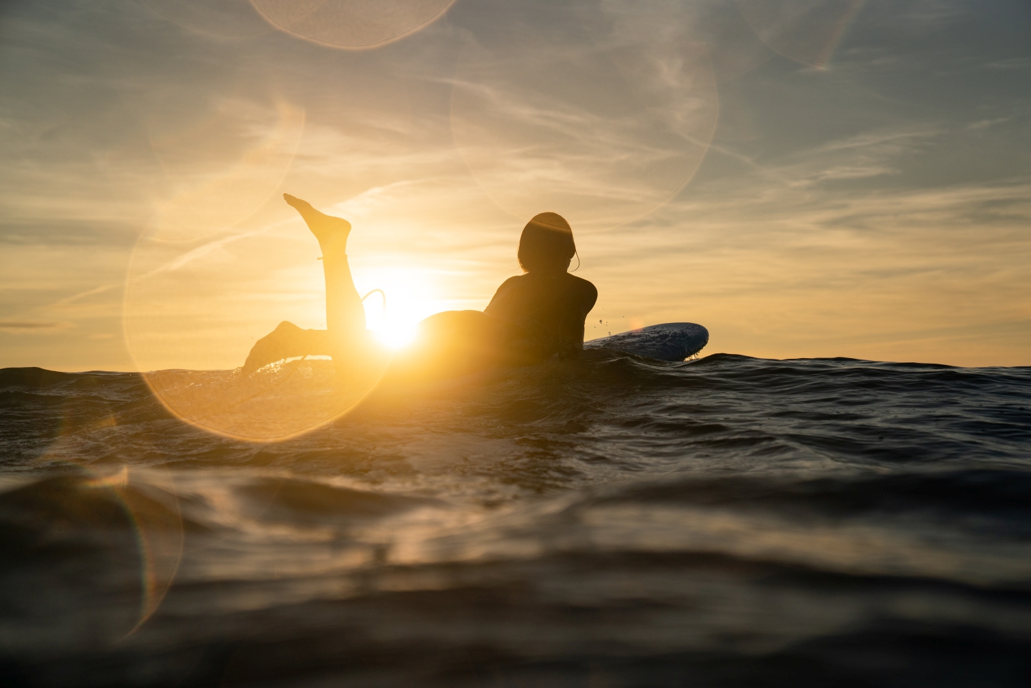 Silhouette of woman on surfboard with leg in the air and sunset in the background