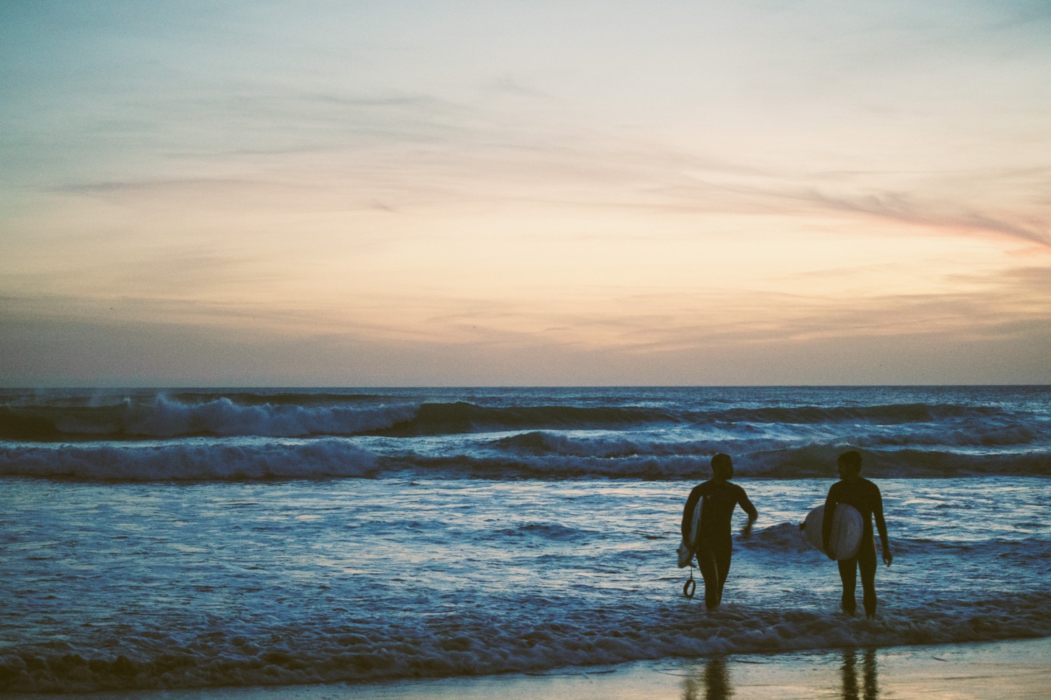 Two men carry surfboards coming out of the sea - Costa de La Luz, Spain