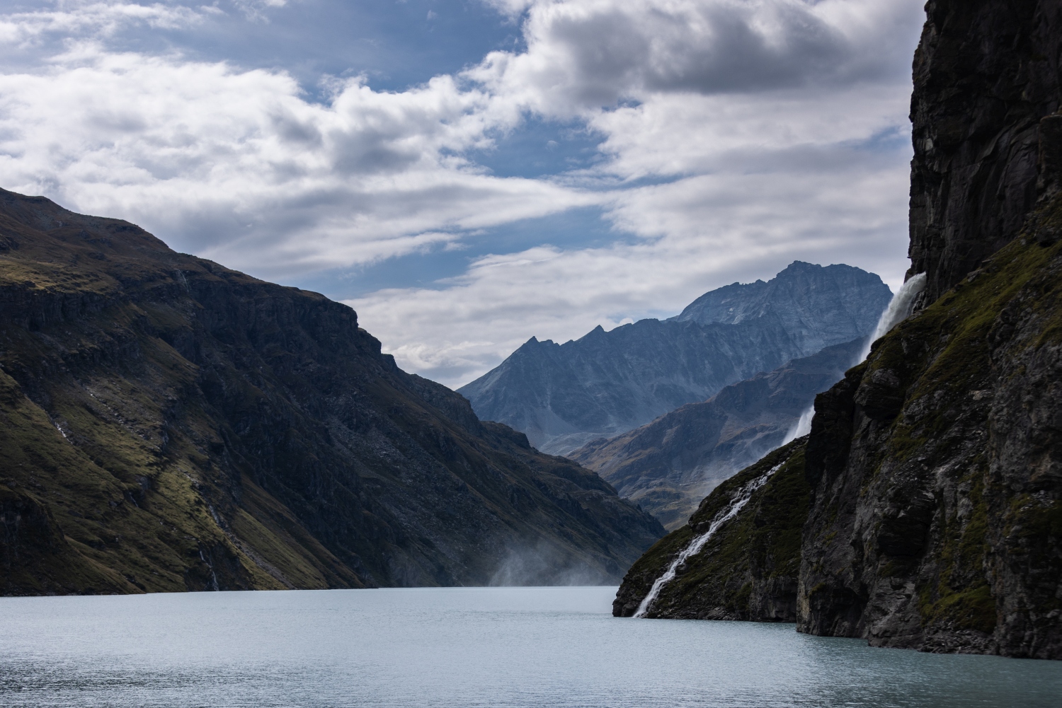 Waterfall spraying into reservoir amongst mountain ranges - Verbier