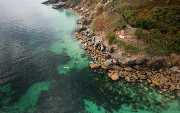 Landscape picture of people kayaking over clear waters next to rocky cliff Brittany CREDIT Jake McKenna