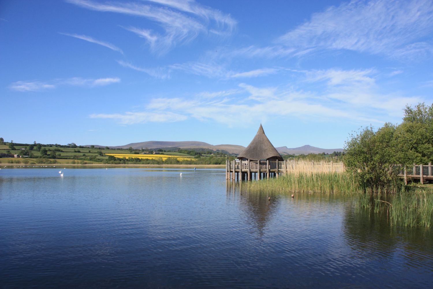 Hut next to lake with mountains and blue sky in background, Brecon Beacons 