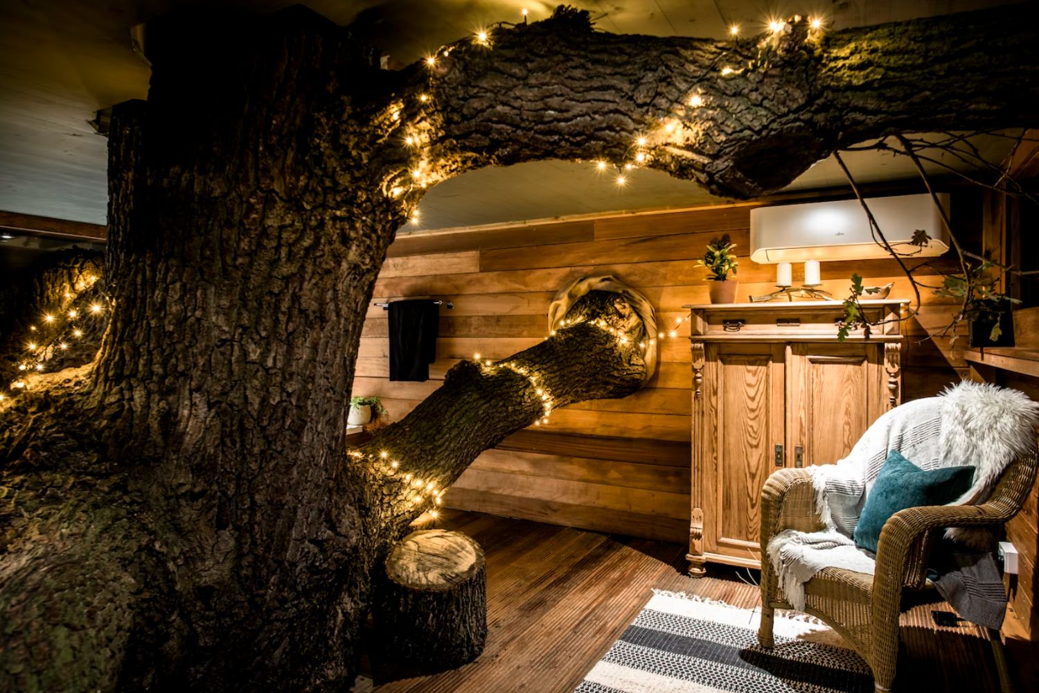 Treehouse living with tree with fairy lights growing through it - The Old Oak Treehouse, Coleman’s Farm, Essex, England