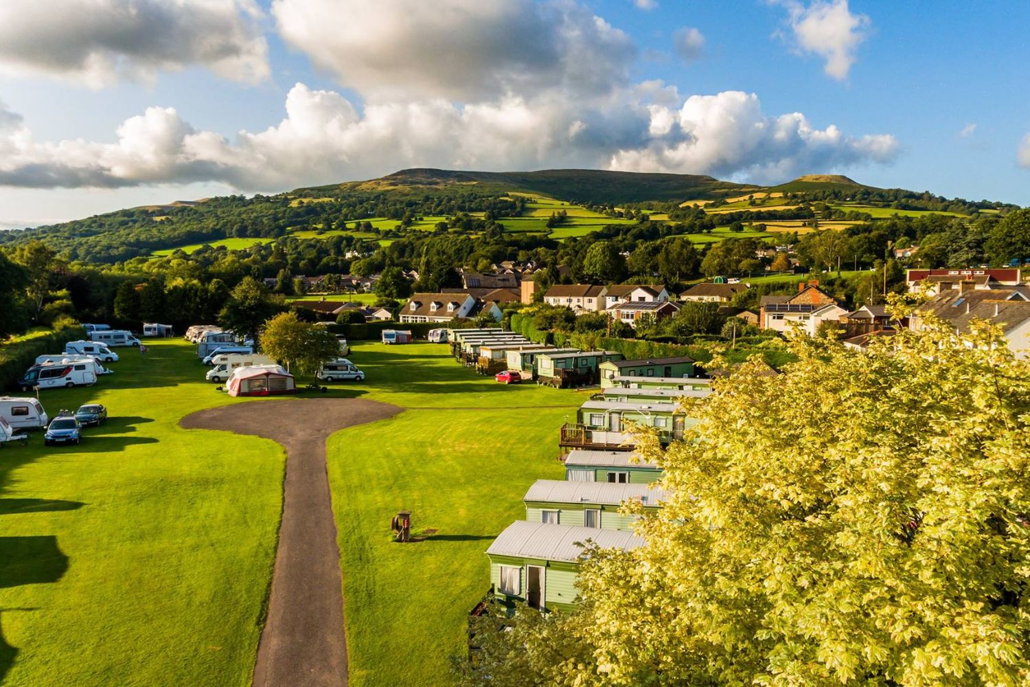 View of campsite with car, campers and caravans parked with green hills in background, Brecon Beacons