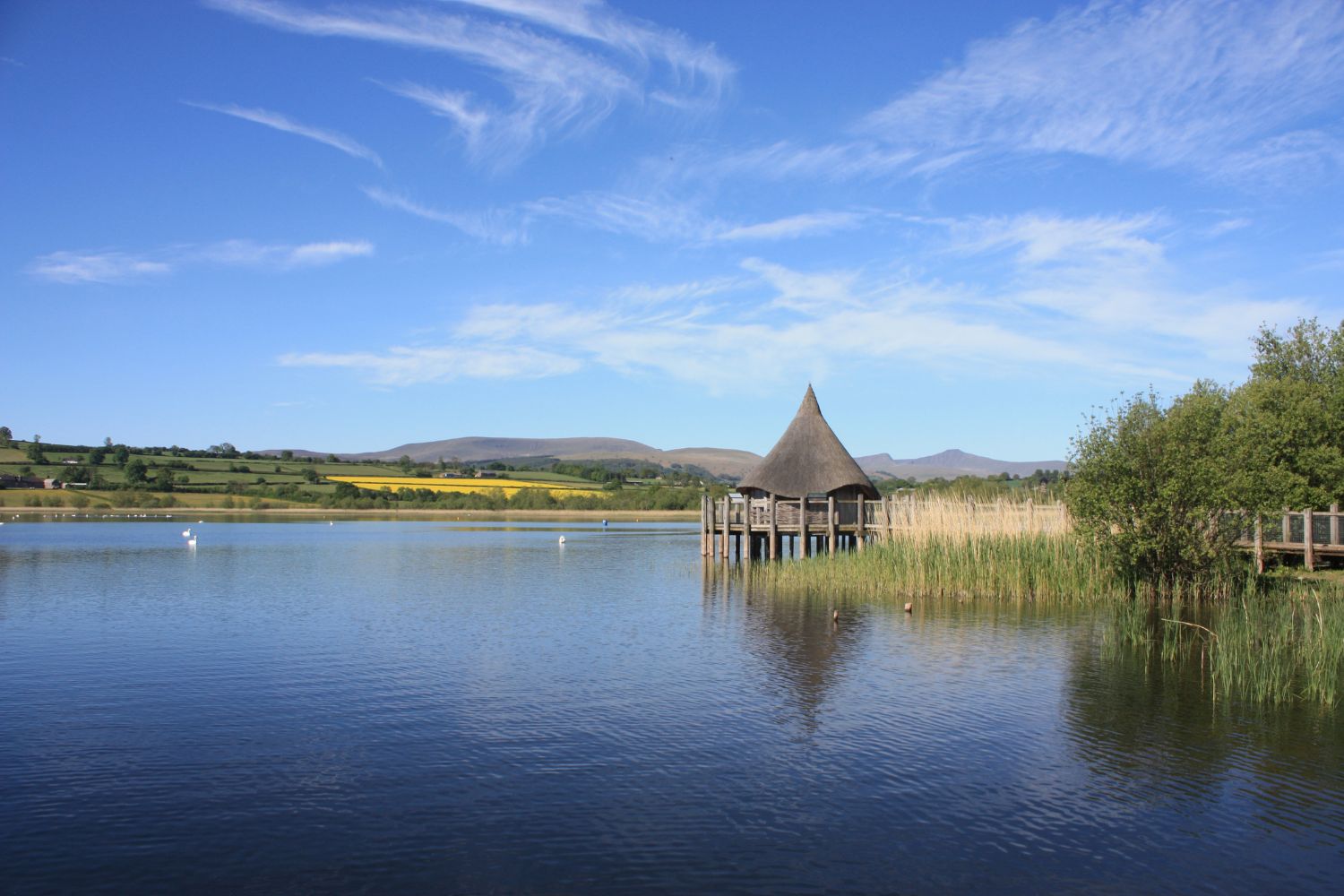 Hut next to lake with mountains and blue sky in background, Brecon Beacons